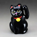 Black cat figurine with yellow eyes and red bow tie on a gray background.