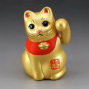 Gold cat figurine with red bib and paw raised on a gray background.