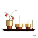 Decorative setup with gold containers, a candle, and a branch on a white background.